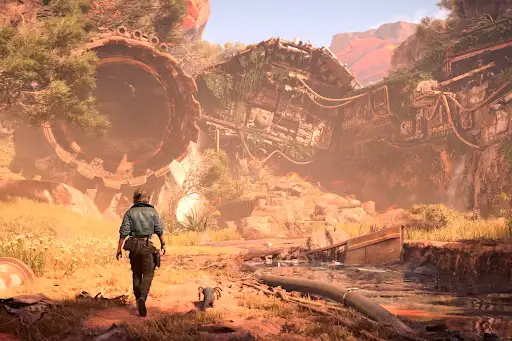 Un hombre camina hacia una estructura circular grande en un paisaje con escombros, vegetación y montañas distantes.