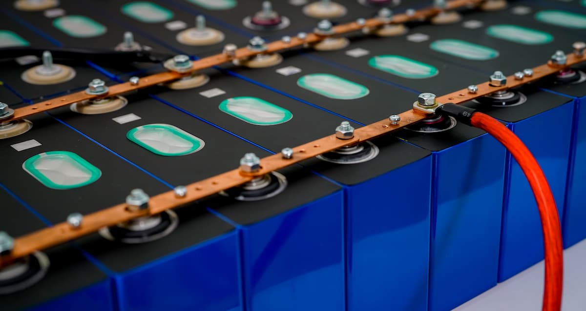 Módulo de baterías de litio con celdas prismáticas azules conectadas por barras de cobre y cable rojo.