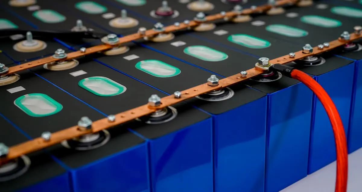 Módulo de baterías de litio con celdas prismáticas azules conectadas por barras de cobre y cable rojo.