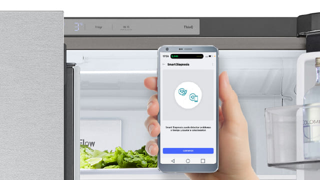 Mano con smartphone usando app para diagnosticar el refrigerador abierto.