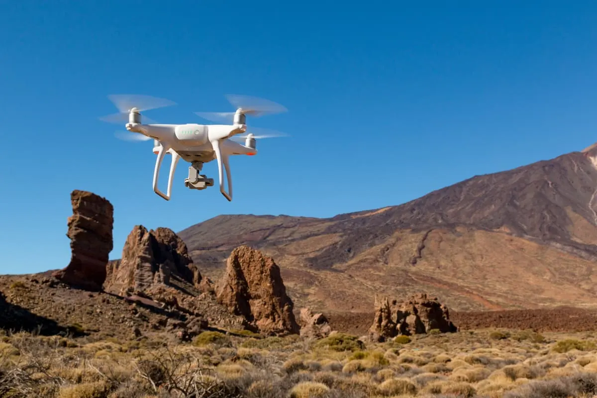 Dron blanco volando sobre un paisaje árido de montañas y rocas.