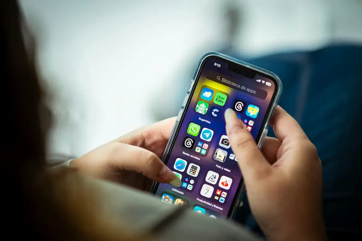 Mano sosteniendo un teléfono inteligente con la pantalla mostrando iconos de aplicaciones en categorías como redes sociales y utilidades.