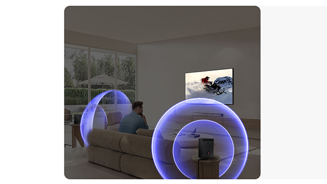 Hombre sentado en sofá viendo la televisión, rodeado de efectos visuales azules que representan sonido envolvente en la sala moderna.