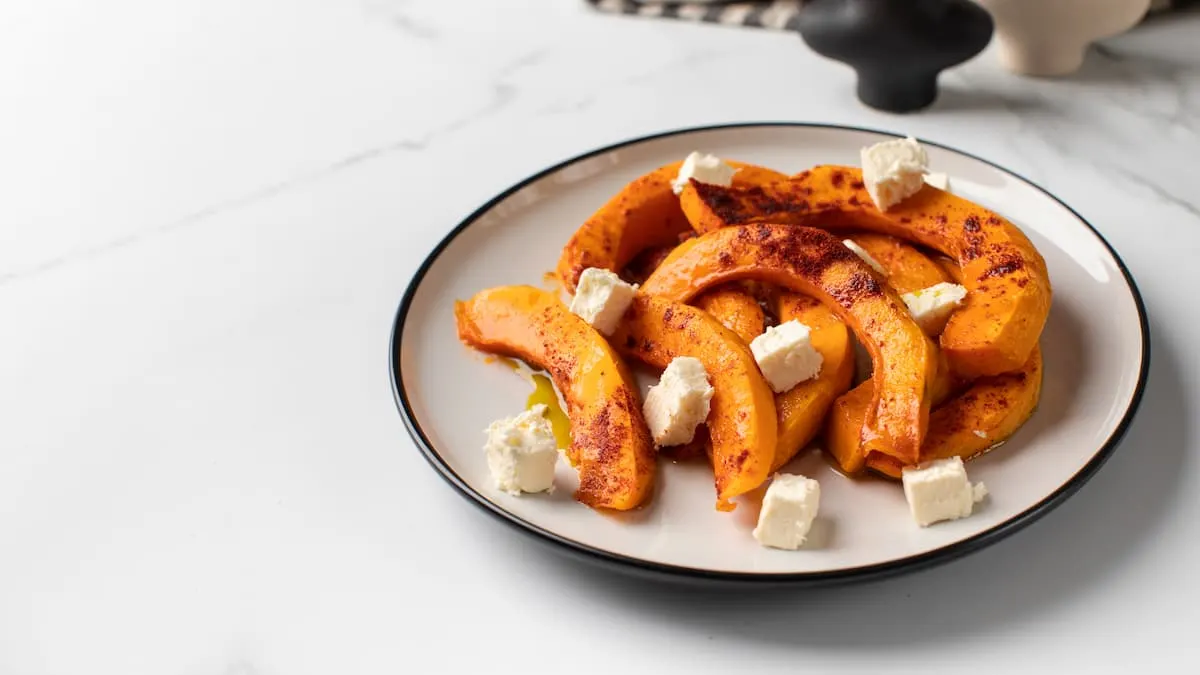 Rodajas de calabaza asada con trozos de queso blanco en un plato blanco.