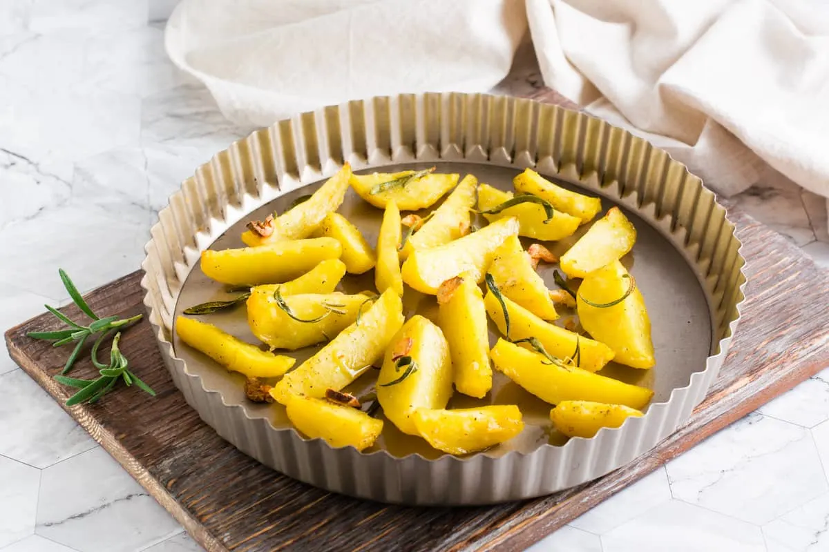 Patatas al horno con romero en un molde redondo sobre tabla de madera.
