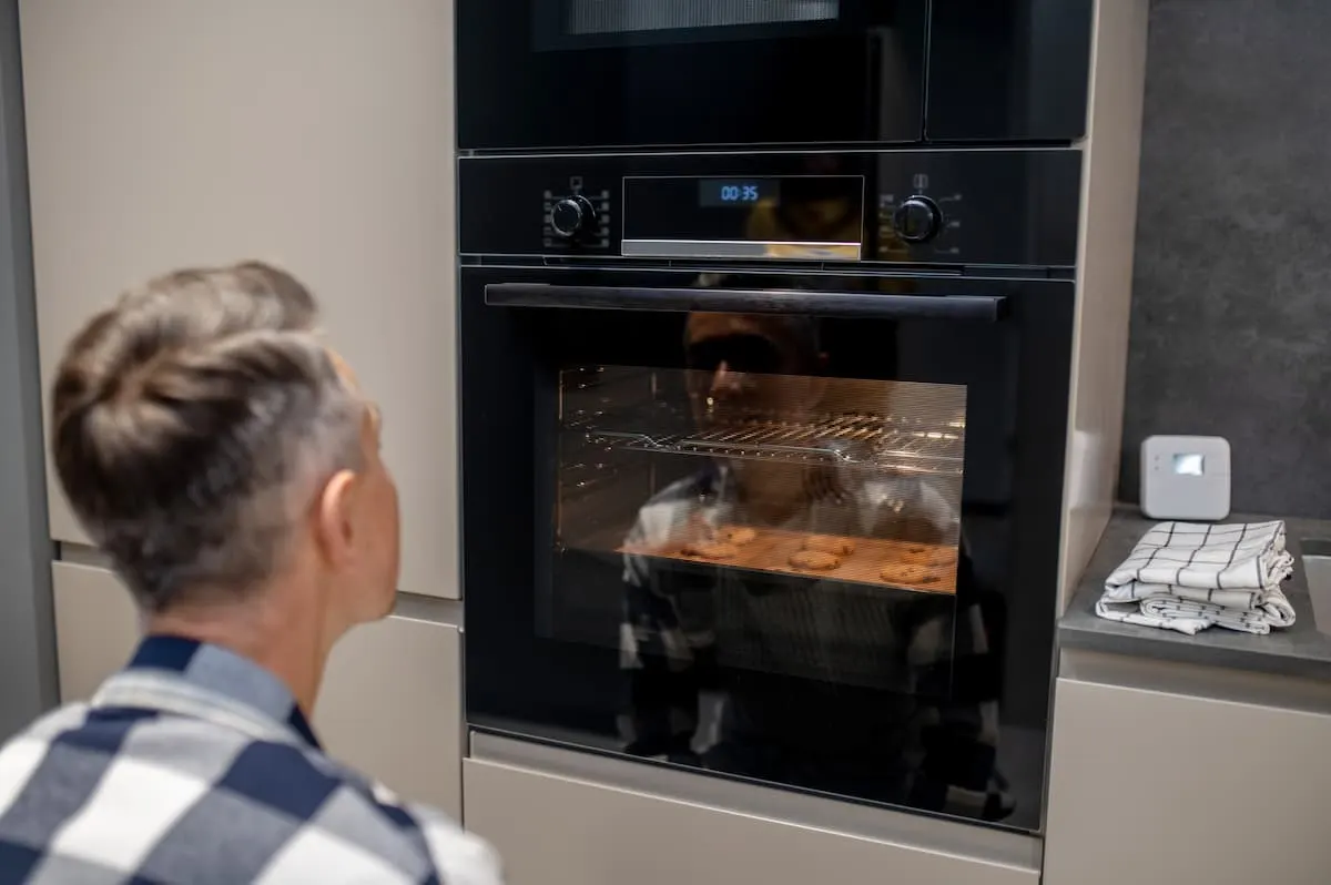 Hombre observando la cocción de galletas en un horno eléctrico empotrado.