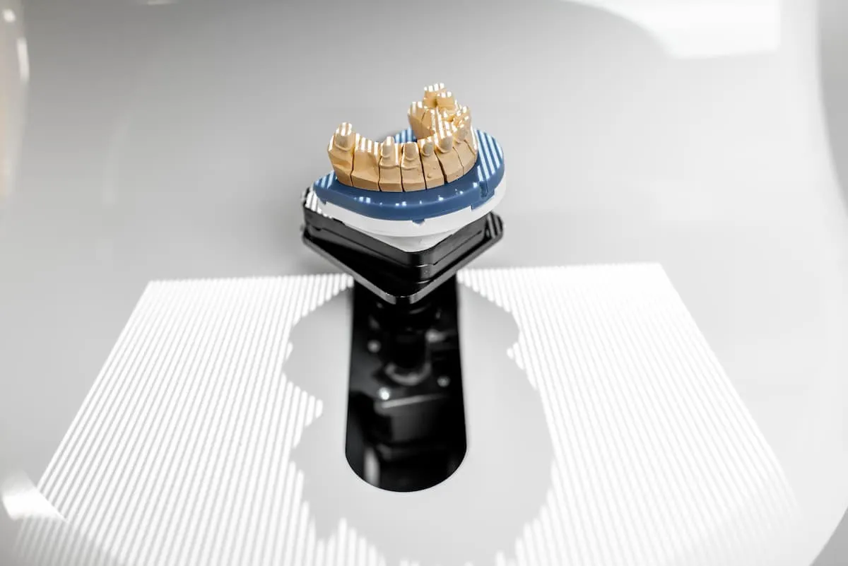 Modelo dental siendo escaneado en un dispositivo 3D sobre una superficie blanca.