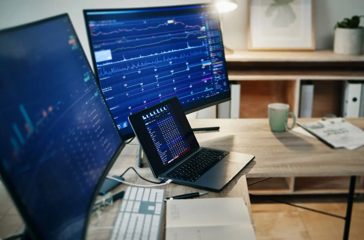 Estación de trabajo con varios monitores y portátil mostrando gráficos financieros.