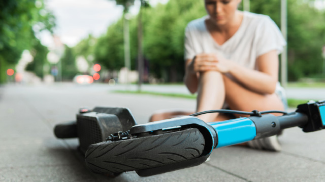 Persona sentada en la acera tras caerse de un patinete eléctrico.