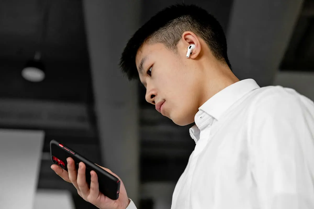 Joven usando auriculares inalámbricos mientras mira su móvil