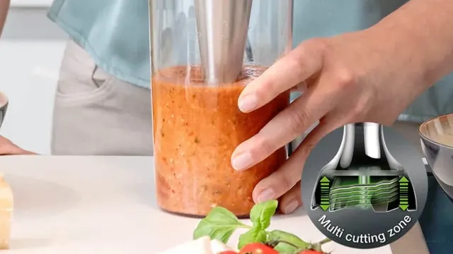Una persona sosteniendo con la mano izquierda un vaso con una mezcla que la mano derecha hace con la minipimer