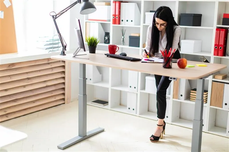 Mujer trabajando de pie en escritorio ajustable en oficina moderna.