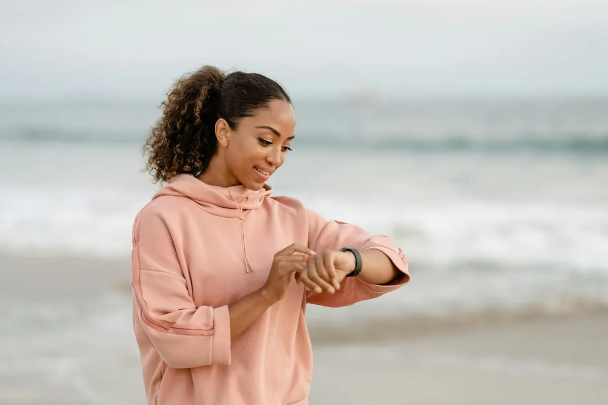 Mujer con sudadera rosa usando un smartwatch en la playa.