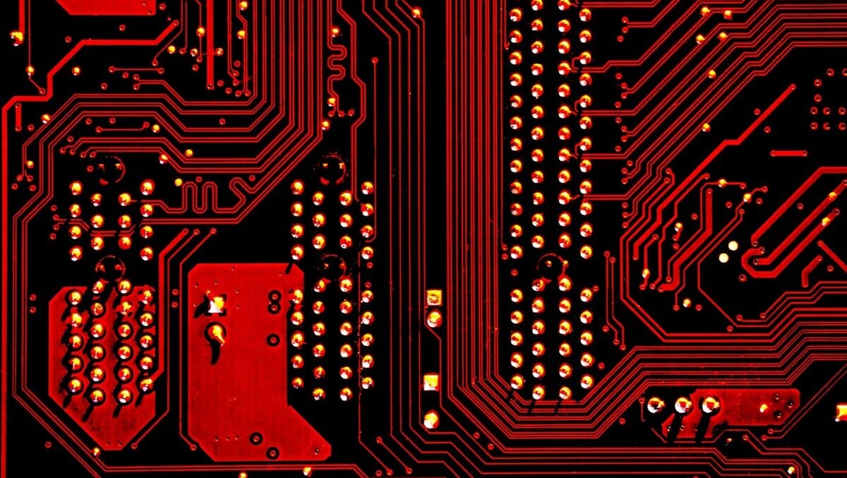 Detalle de placa de circuito en negro con trazos y puntos rojos, mostrando la complejidad de su diseño electrónico.