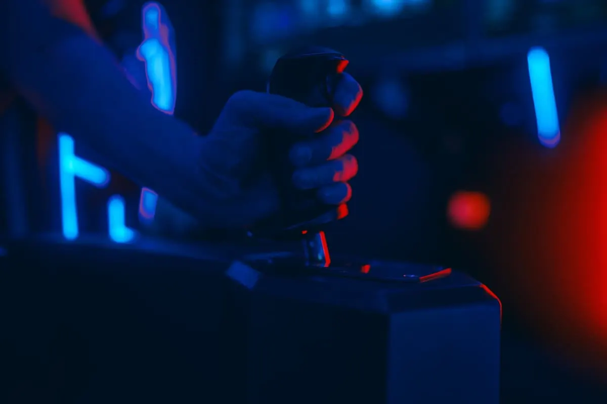 Mano sujetando un joystick de control en un entorno oscuro con luces azules y rojas