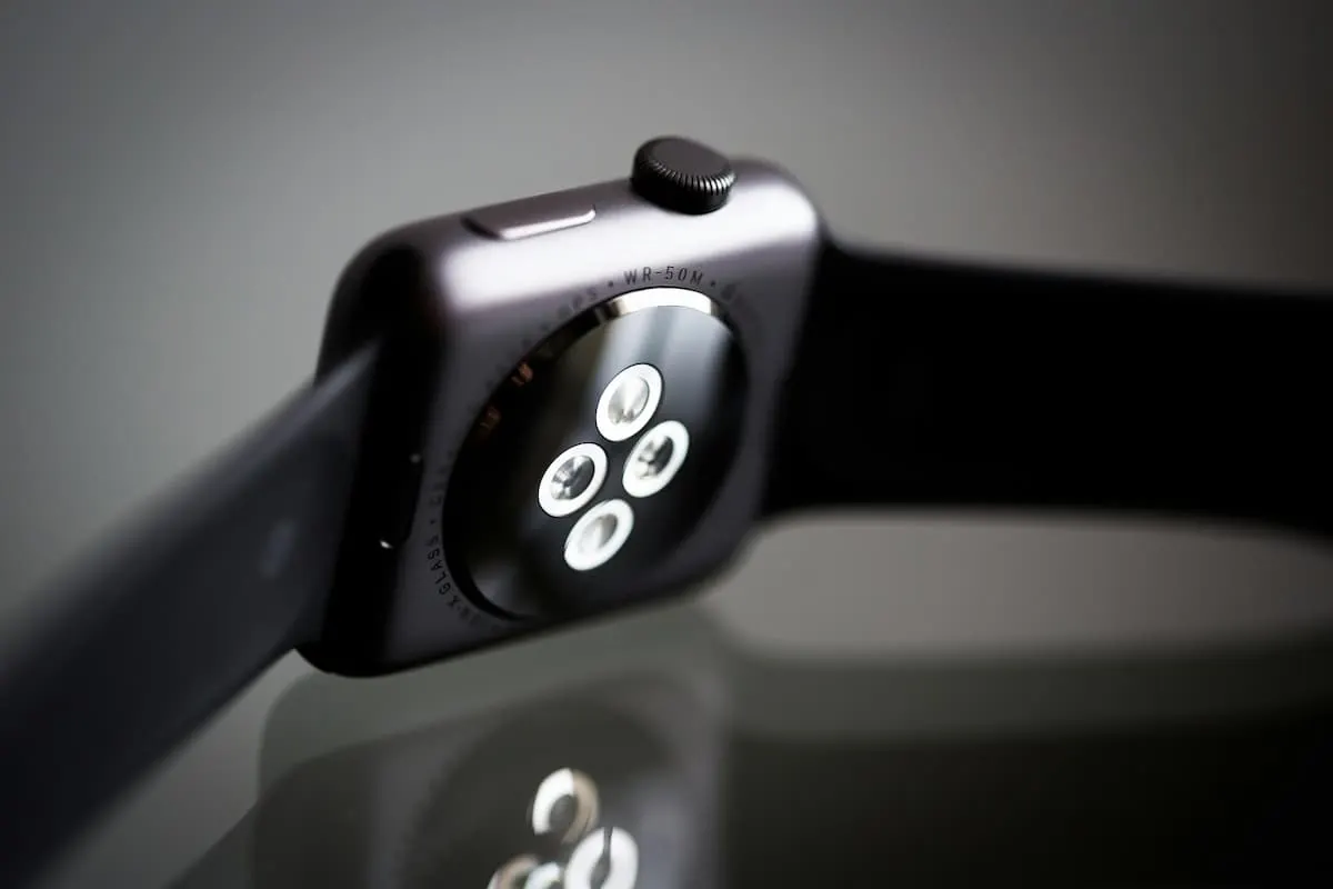 Parte trasera de un smartwatch negro sobre superficie reflectante.