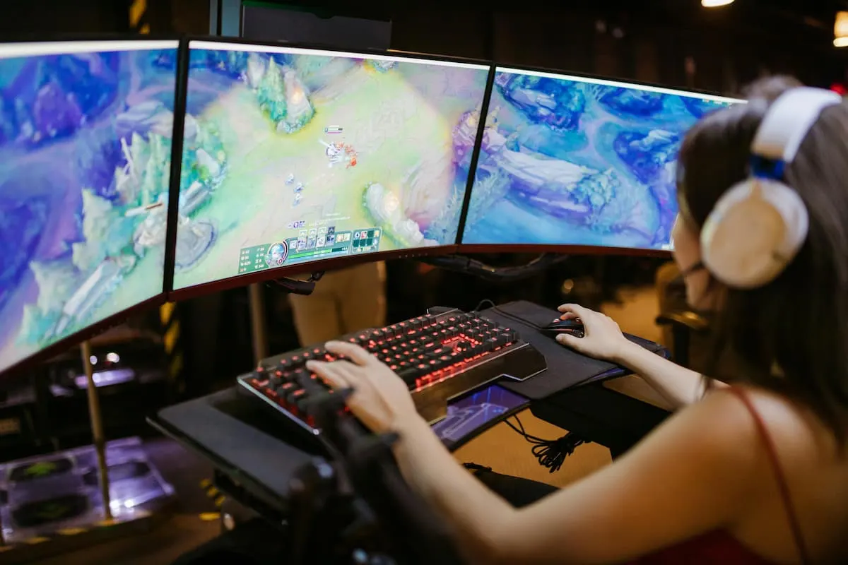 Persona jugando en un setup con tres monitores y auriculares.