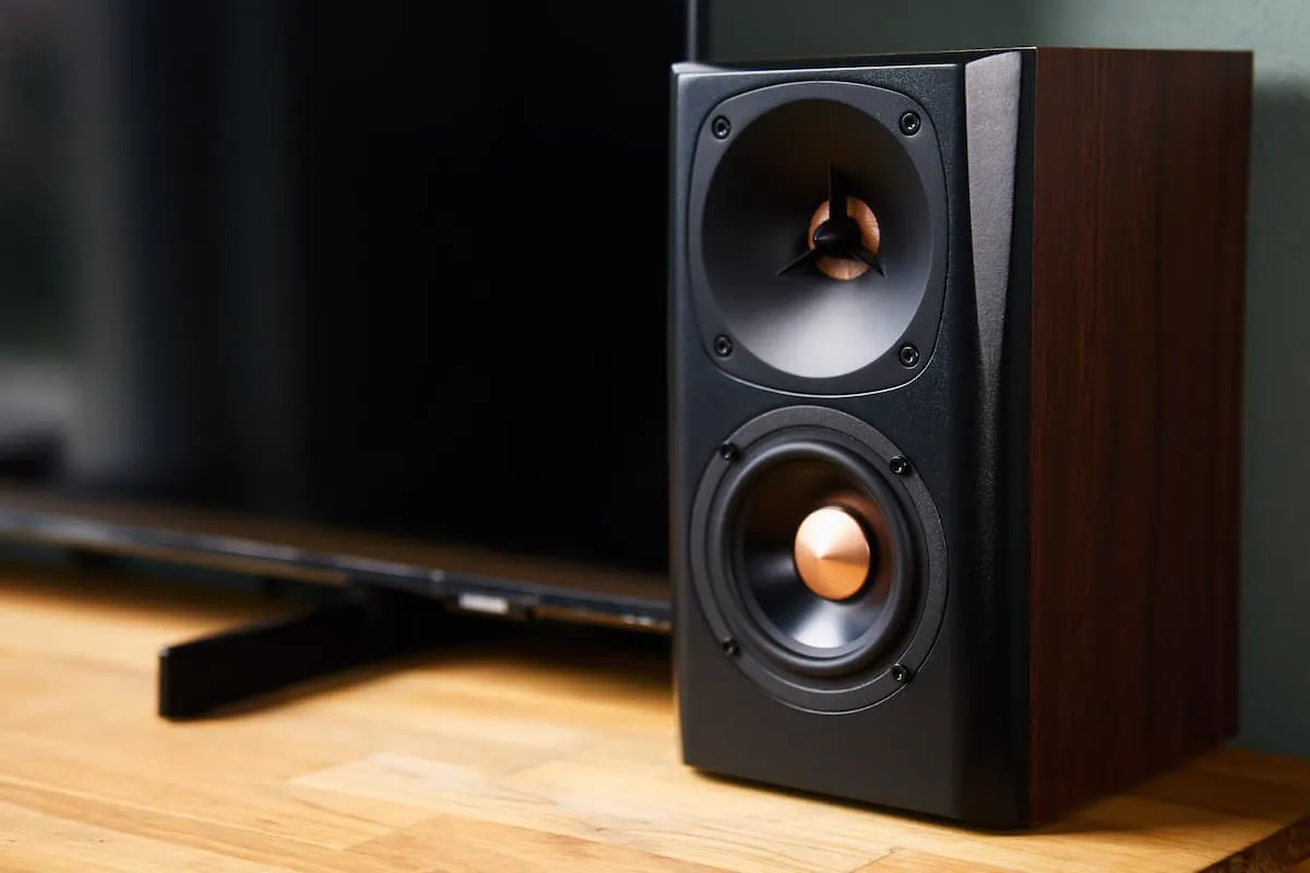 Altavoz de estantería con acabado en madera junto a un televisor, ideal para mejorar el sonido al ver el fútbol en casa