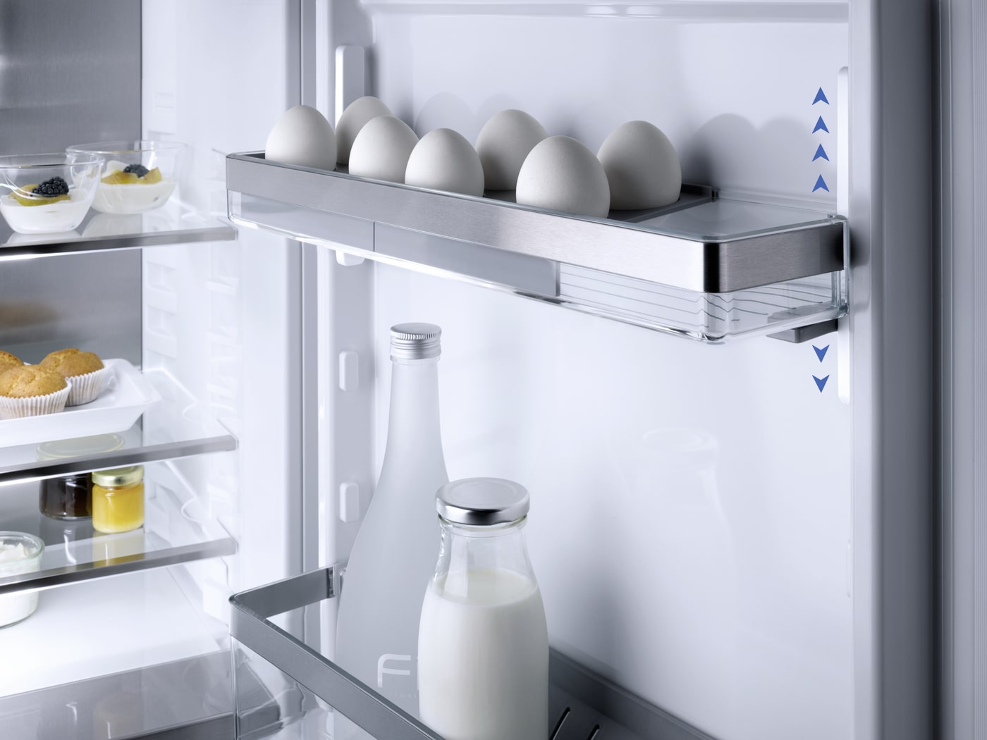 Interior de un refrigerador con huevos en un estante superior, botellas de leche y postres en estantes inferiores.
