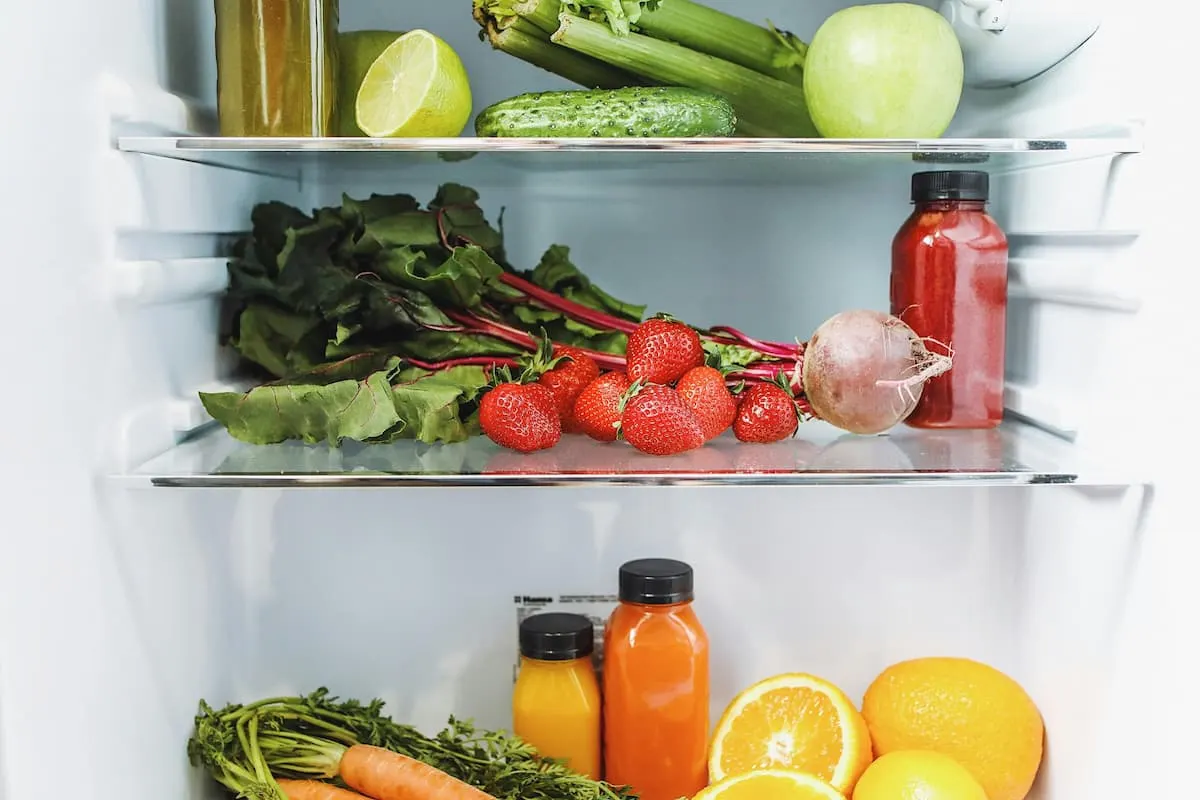 Frigorífico ordenado con frutas, verduras y botellas de zumo natural en los estantes.