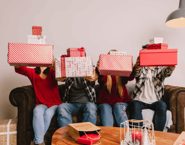 Grupo de personas sentadas en un sofá sosteniendo cajas de regalos navideños envueltos en rojo y blanco, imagen festiva ideal para una landing de regalos.