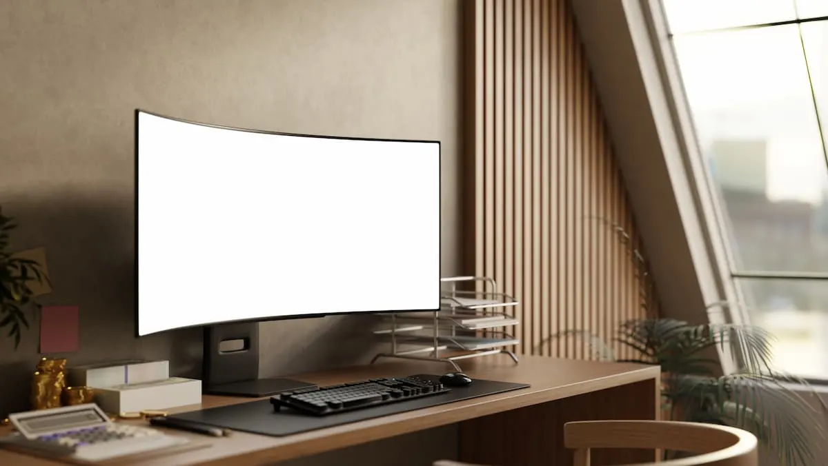 Escritorio de madera con monitor curvo en blanco, teclado y decoración minimalista junto a una ventana.