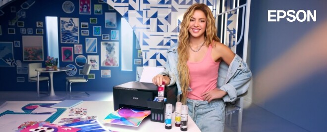 Mujer usando impresora Epson EcoTank en estudio creativo, rellenando tinta junto a impresiones a color y botellas de tinta.