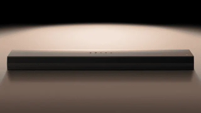 Una barra rectangular negra con pequeños orificios en la parte superior está sobre una superficie lisa. El fondo es oscuro.