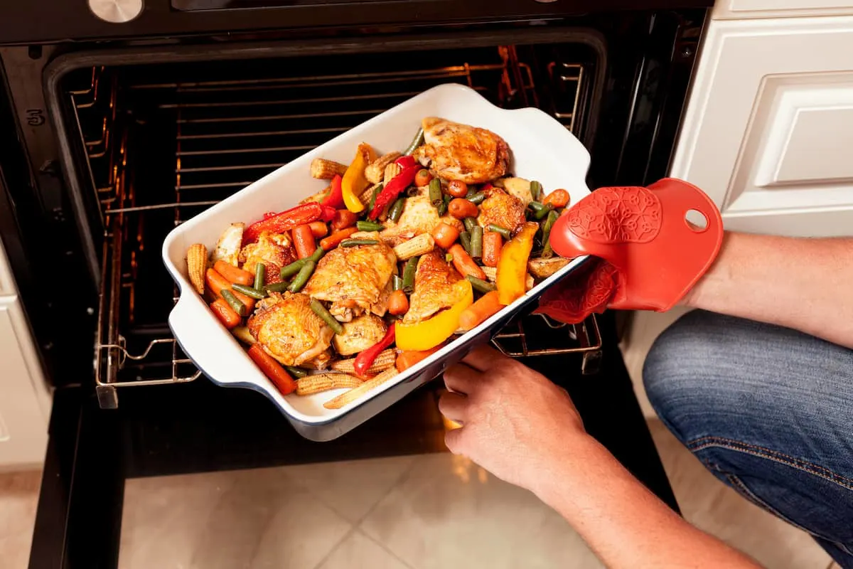 Persona sacando una bandeja con pollo y verduras del horno.