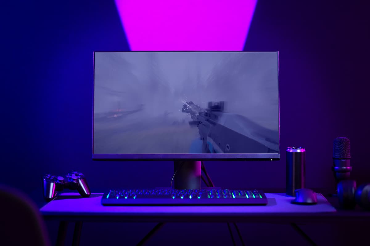 Setup gamer con monitor mostrando videojuego de disparos, teclado RGB y luz ambiental morada.