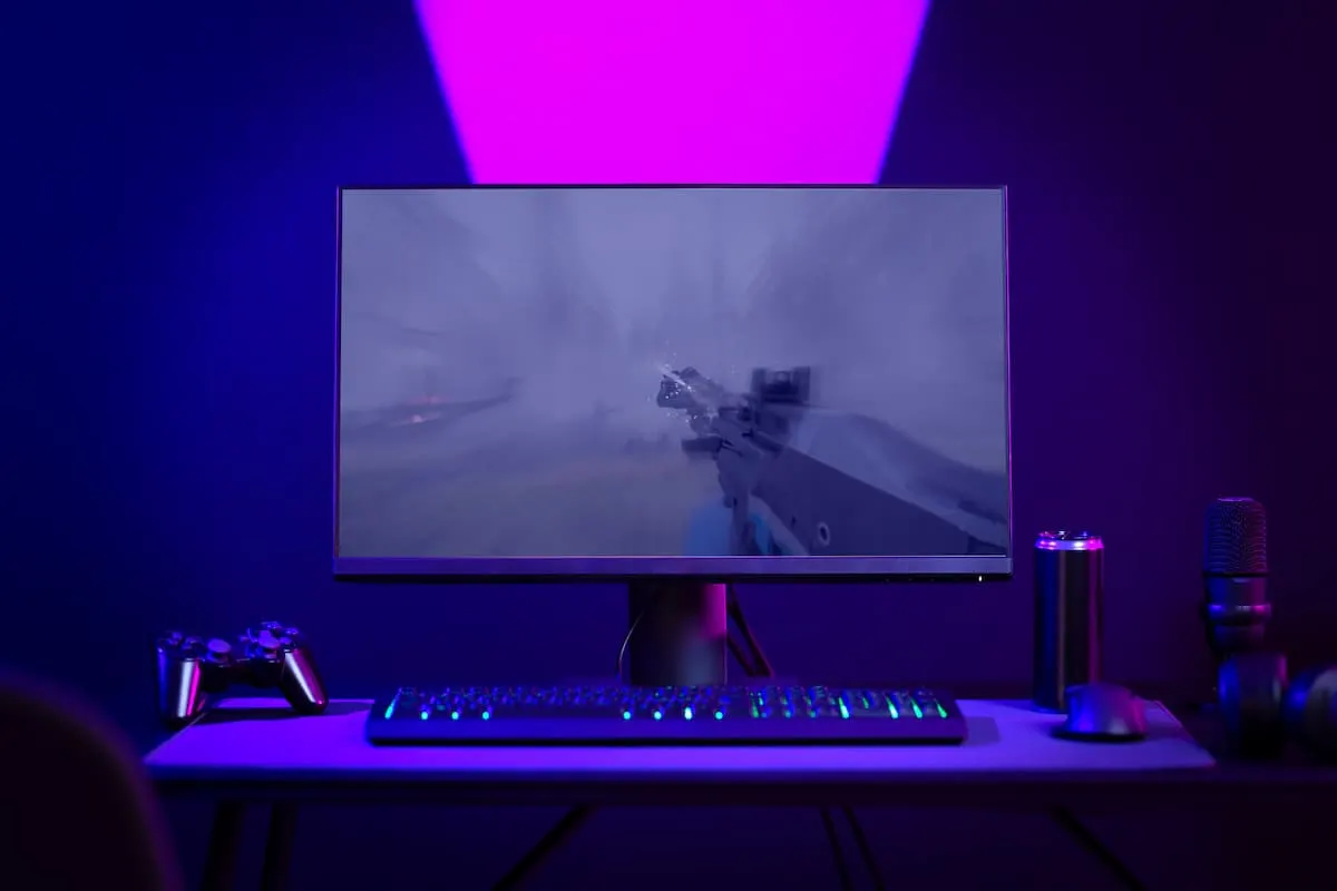 Setup gamer con monitor mostrando videojuego de disparos, teclado RGB y luz ambiental morada.