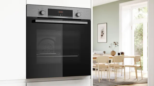 Primer plano del horno instalado en alto en un mueble blanco. Al fondo, un luminoso comedor conectado con la cocina