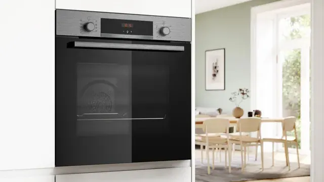 Primer plano del horno instalado en alto en un mueble blanco. Al fondo, un luminoso comedor conectado con la cocina