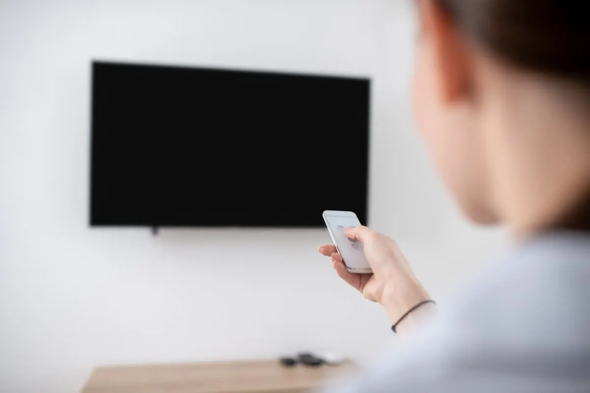 Persona usando el mando frente a un televisor apagado