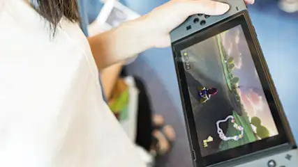 Una persona sostiene una consola Nintendo Switch gris que muestra un juego de carreras en su pantalla.