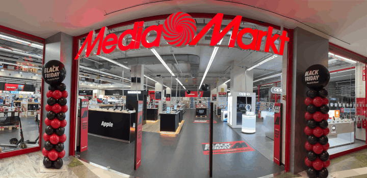 Entrada a Media Markt con rótulo rojo y globos de Viernes Negro. Dentro, mostradores con productos electrónicos.