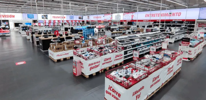 Vista interior de una tienda con secciones de televisión y electrónica, con estanterías y ofertas especiales en palés.