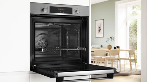 Primer plano del horno instalado en alto en un mueble blanco. Al fondo, un luminoso comedor conectado con la cocina