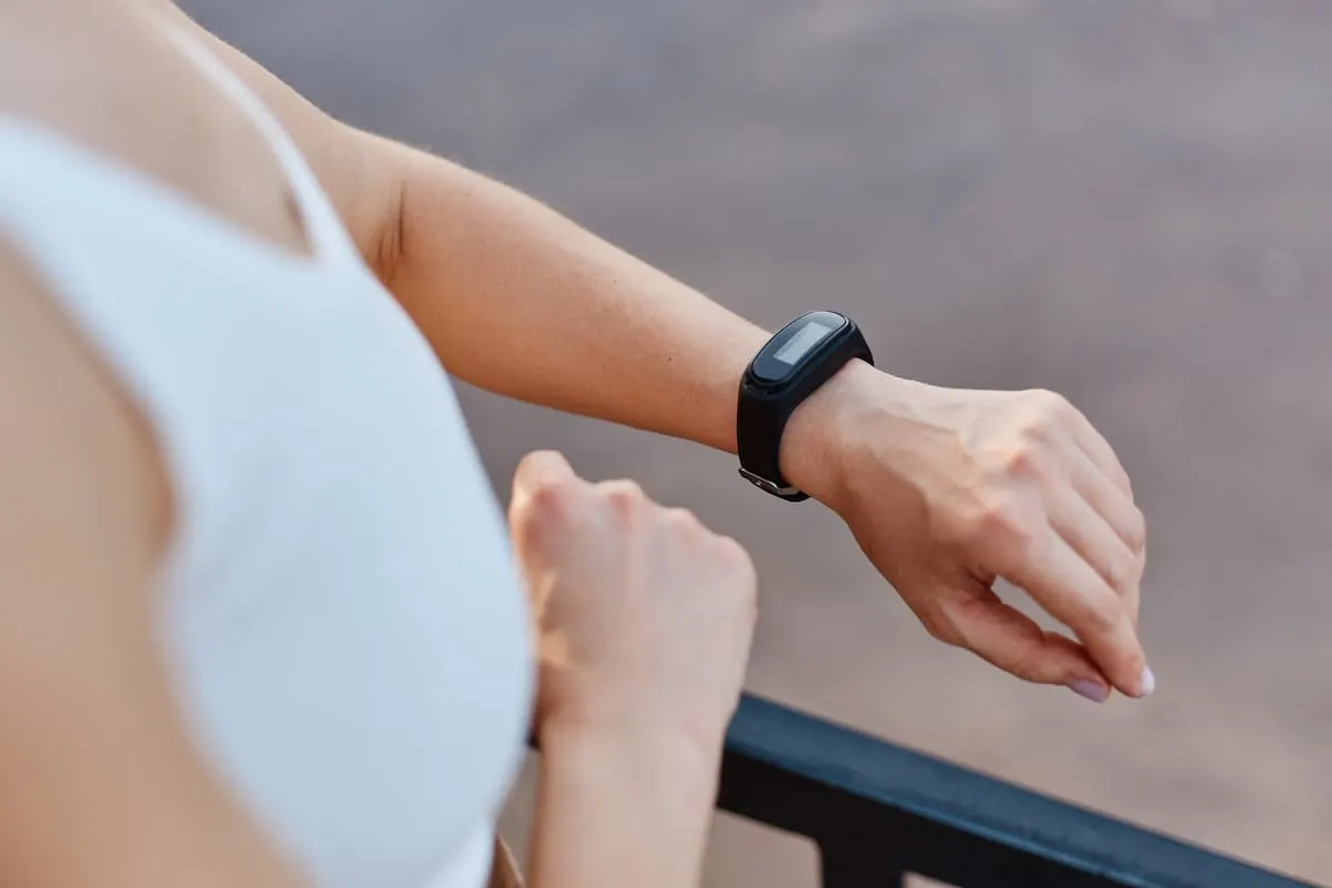 Imagen de una chica vestida con ropa de deporte, plano destacado de la muñeca con una pulsera de actividad de color negro.