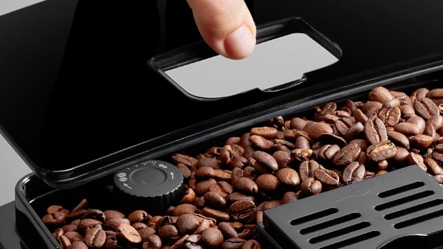 Mano abriendo compartimento de café en grano de la cafetera.
