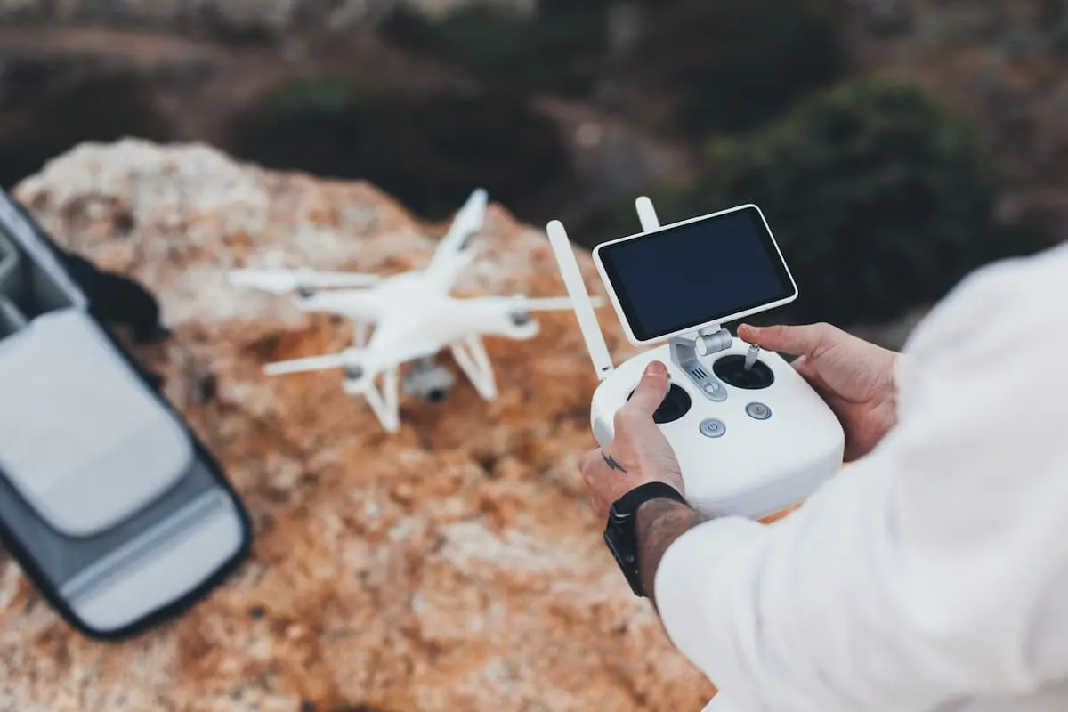 Persona controlando un dron con mando y pantalla en un entorno rocoso al aire libre.
