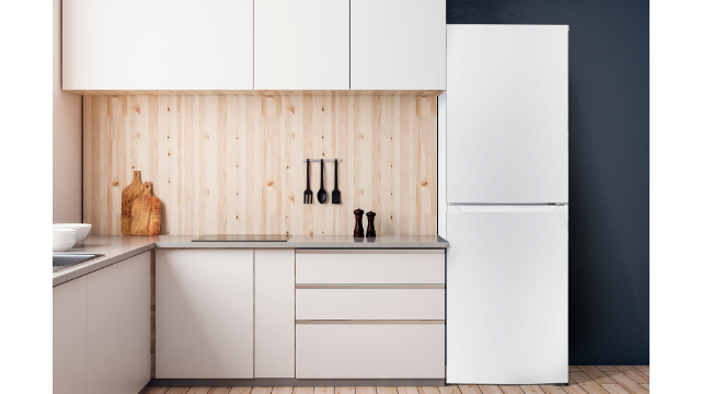 Cocina con armarios y encimera blancos, frigorífico blanco, utensilios negros y pared de madera clara con fondo azul oscuro.