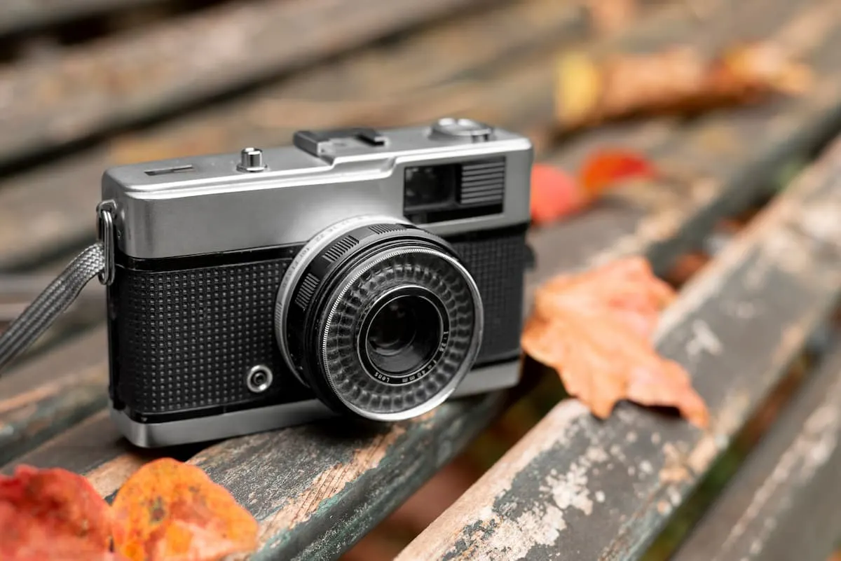 Cámara fotográfica clásica sobre un banco de madera, rodeada de hojas secas de otoño.