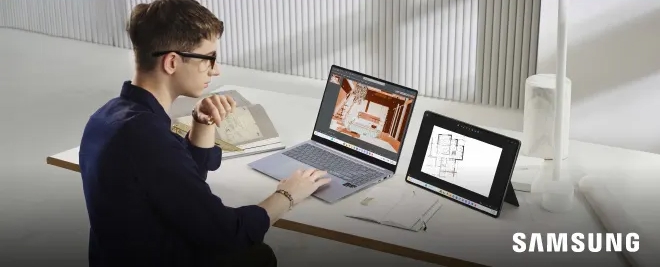 Persona sentada en un escritorio trabajando con una laptop Samsung y una tablet Samsung, revisando planos arquitectónicos, con materiales de oficina alrededor.