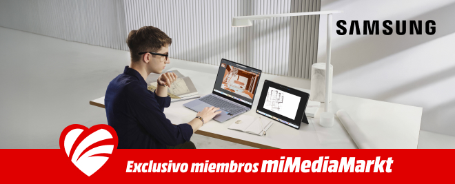 Persona sentada en un escritorio trabajando con una laptop Samsung y una tablet Samsung, revisando planos arquitectónicos, con materiales de oficina alrededor.