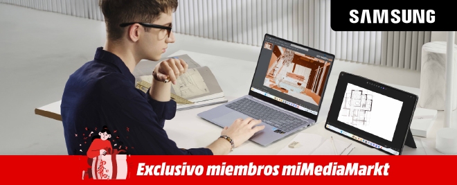 Persona sentada en un escritorio trabajando con una laptop Samsung y una tablet Samsung, revisando planos arquitectónicos, con materiales de oficina alrededor.