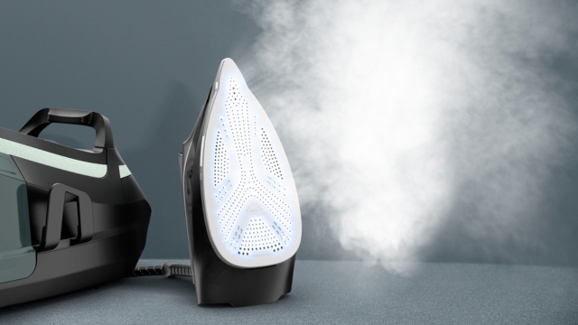 Plancha gris con base de metal perforado junto a un centro de planchado negro sobre una superficie blanca. Al fondo, una ventana.