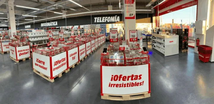 Interior de tienda con pasillos de ofertas en palés con carteles rojos y blancos, secciones de informática y telefonía.
