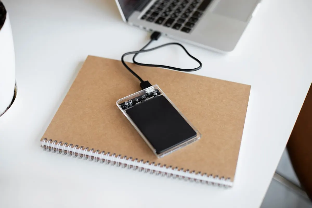 Disco duro externo conectado a un portátil sobre una libreta en un escritorio.