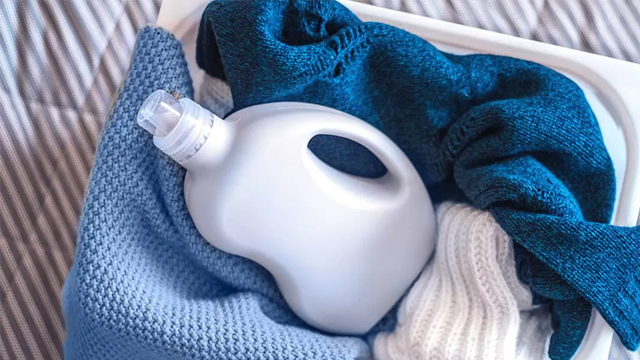 Cesta de ropa con prendas de diferentes tejidos y una botella de detergente